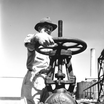 vintage workwear clothing-Worker operating oil pipeline valve, Texaco, TX, USA, 1944.